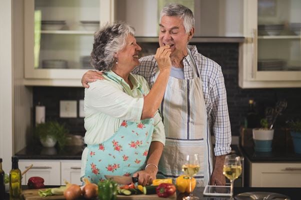 79269751 - smiling senior woman feeding man while standing in kitchen at home